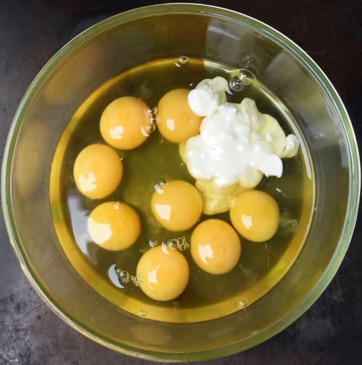 Top down view of 8 raw eggs with yogurt in glass bowl.