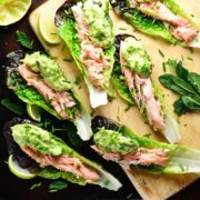 Top down view of lettuce wraps with salmon and guacamole with garnish of herbs on top of wooden board and dark table.