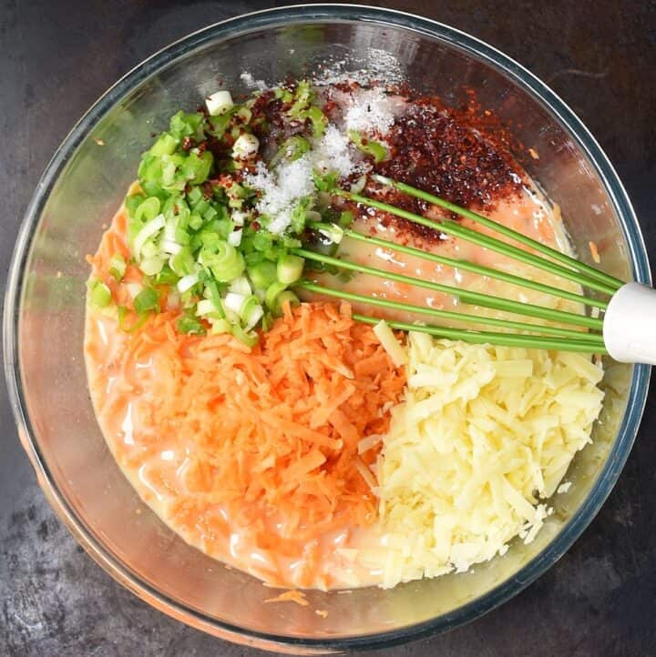 Shredded sweet potato and cheese with chopped scallions and spice in egg mixture with whisk.