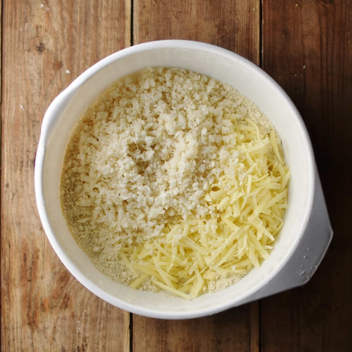 Grated cheese and cauliflower rice with flour inside large white bowl.