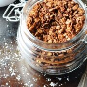 Chocolate granola in open jar with granola in white dish in background.