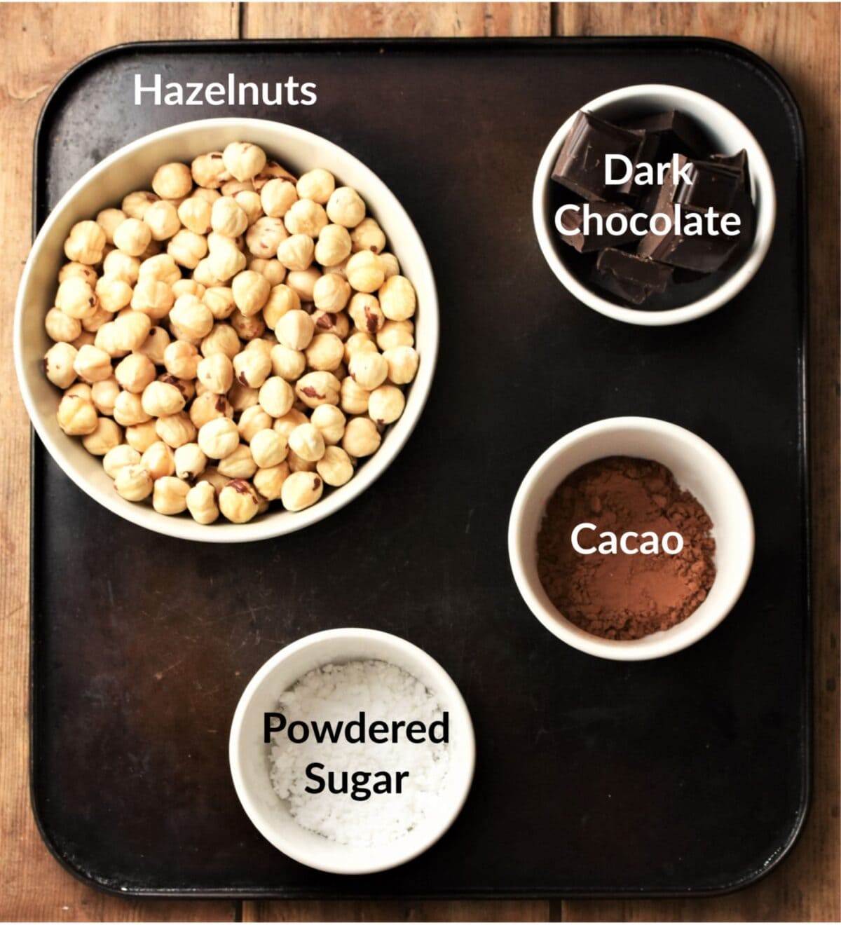 Blanched hazelnuts, icing sugar, chocolate pieces and cocoa in individual bowls.