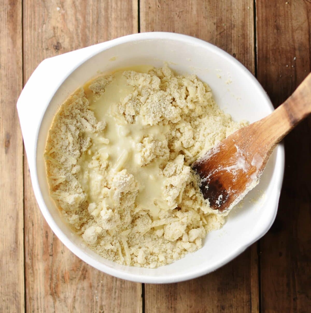Combining flour and buttermilk mixture with wooden spatula inside large white bowl.