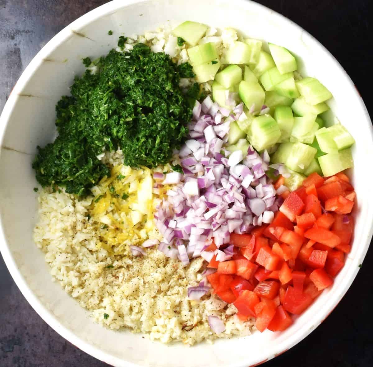 Chopped ingredients for cauliflower tabbouleh salad in large white bowl.