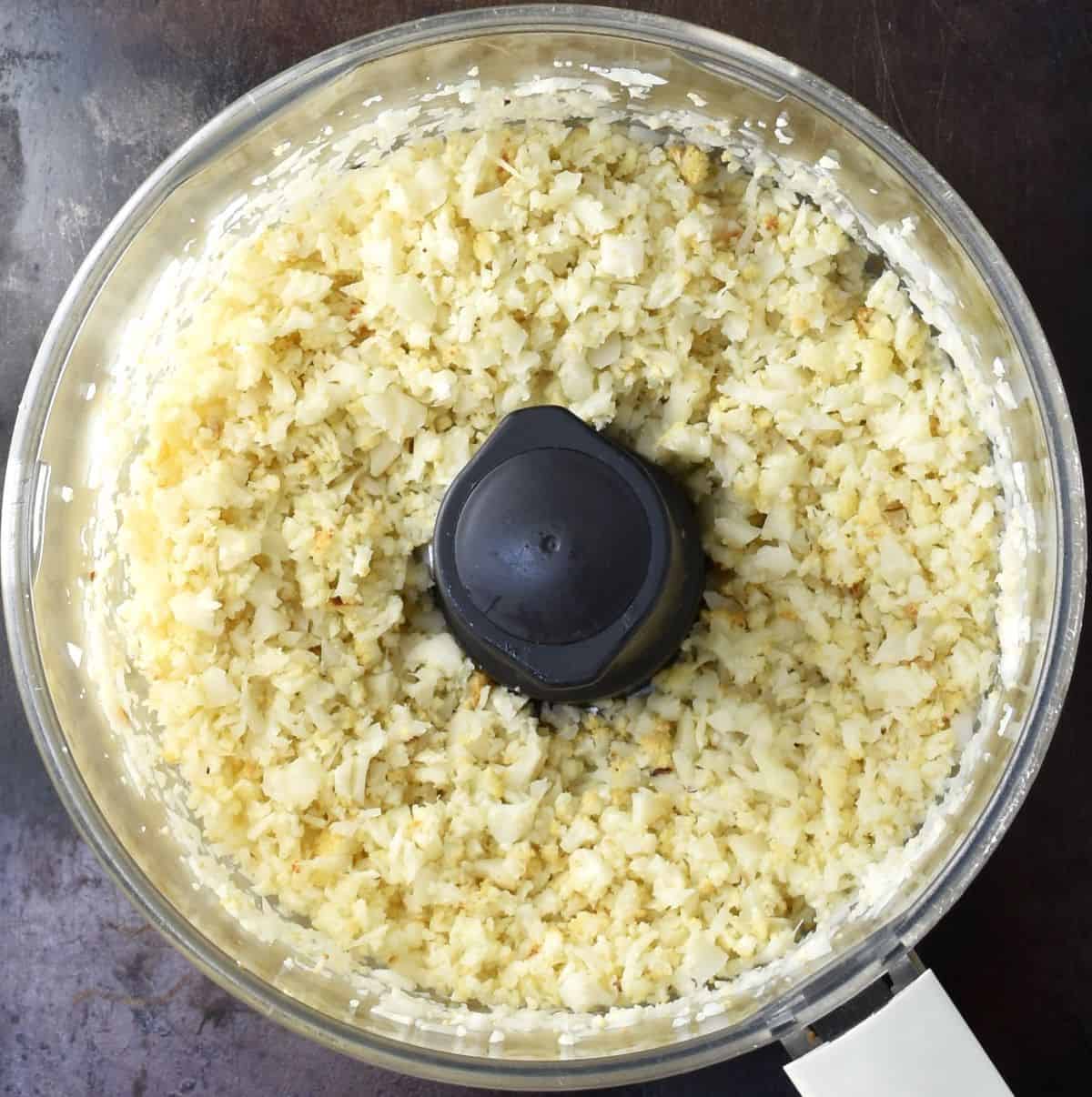 Top down view of chopped cauliflower in food processor bowl.