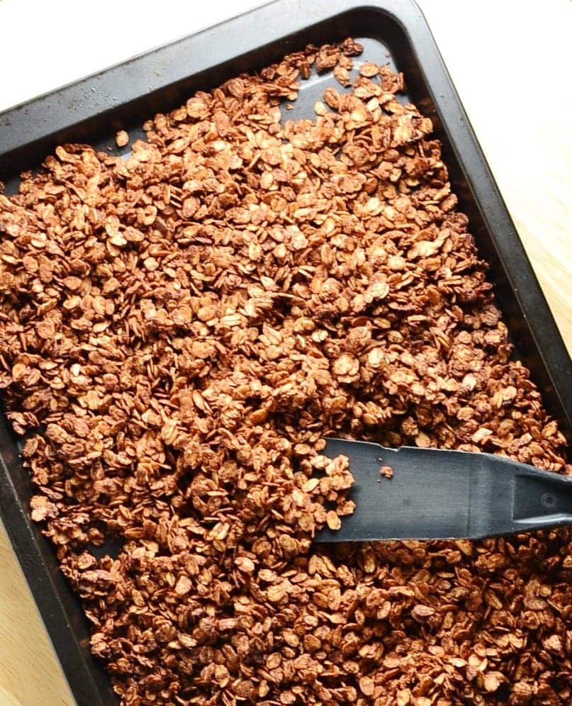 Top down view of chocolate granola on top of baking sheet with black spatula.