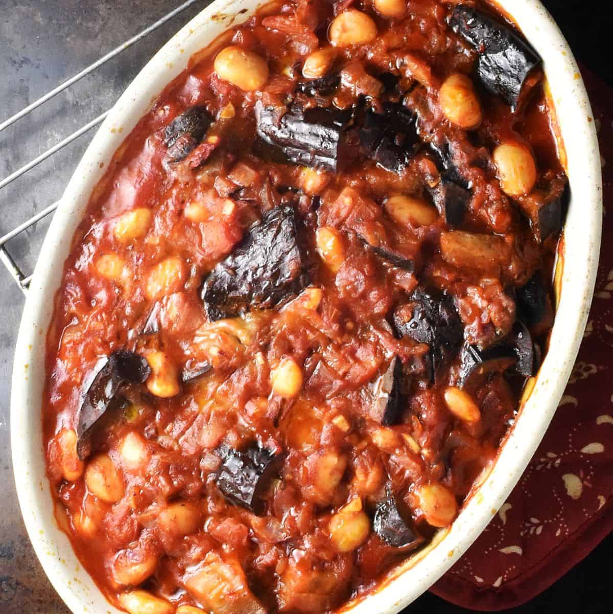 Top down view of eggplant casserole with beans and tomatoes in white oval dish.