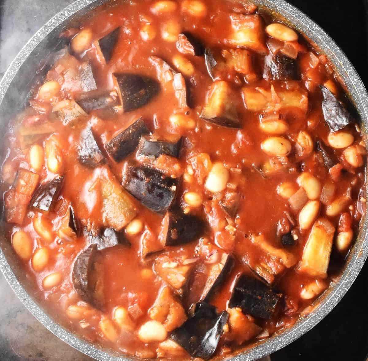 Top down view of eggplant pieces in tomato sauce with beans in large pan.
