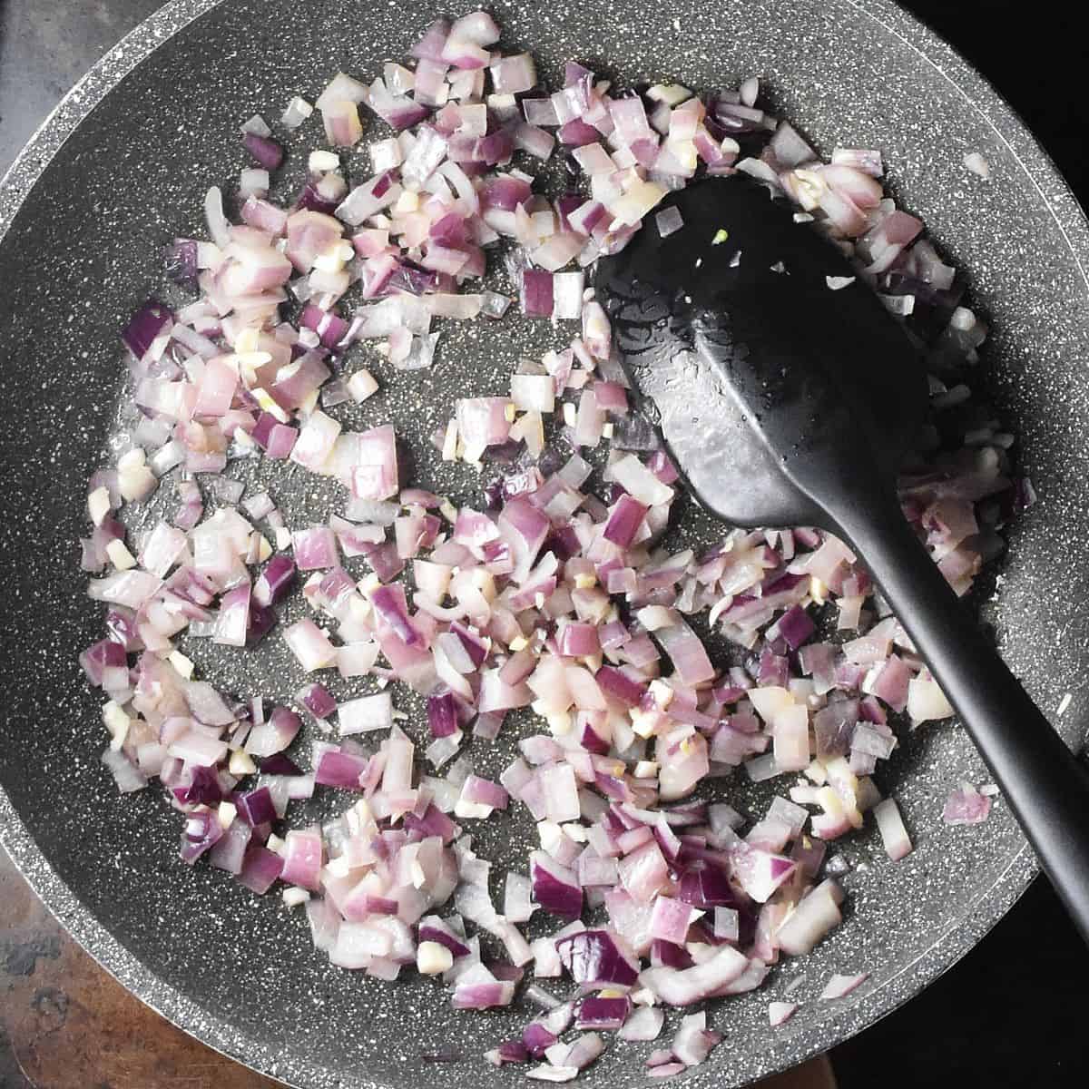 Fried chopped red onion in large pan with black spatula.