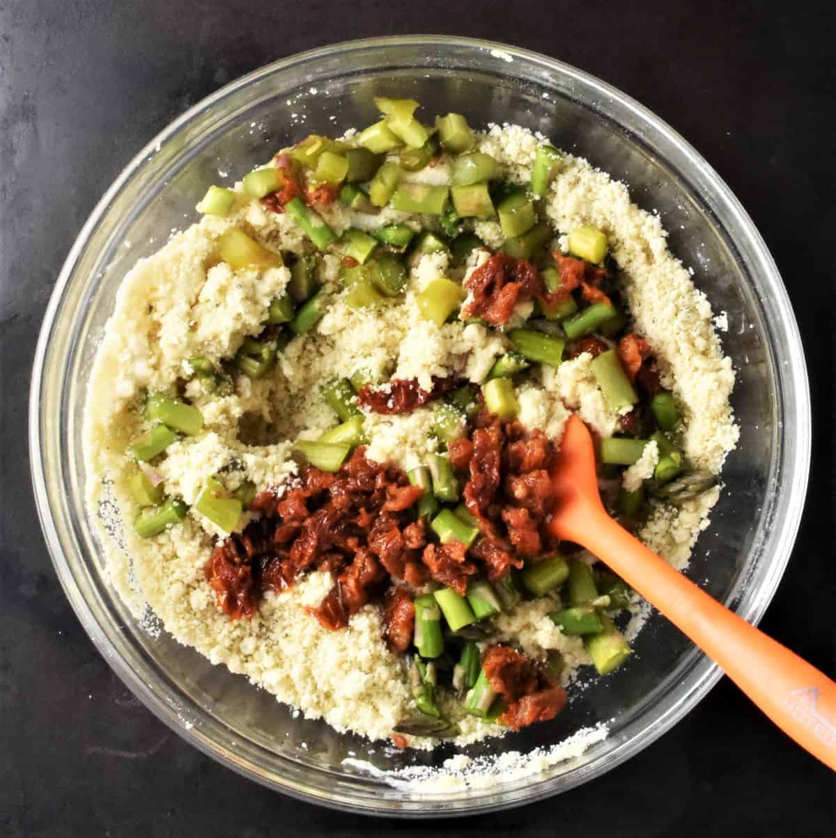 Making scones batter with sundried tomatoes and chopped asparagus in bowl.