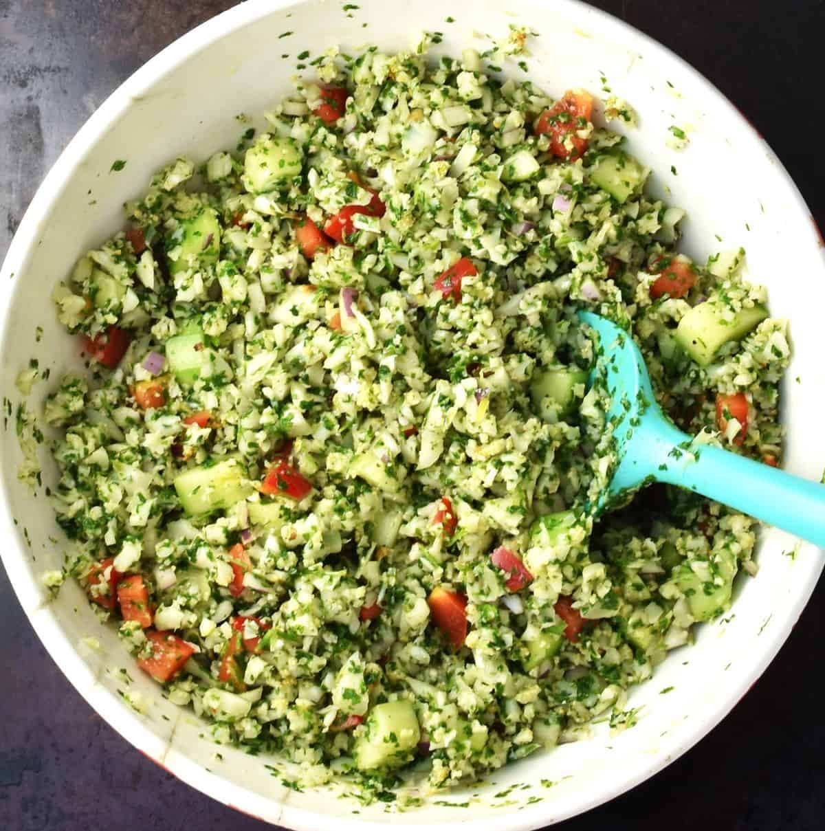Assembled tabbouleh salad with cauliflower in white bowl with blue spoon.