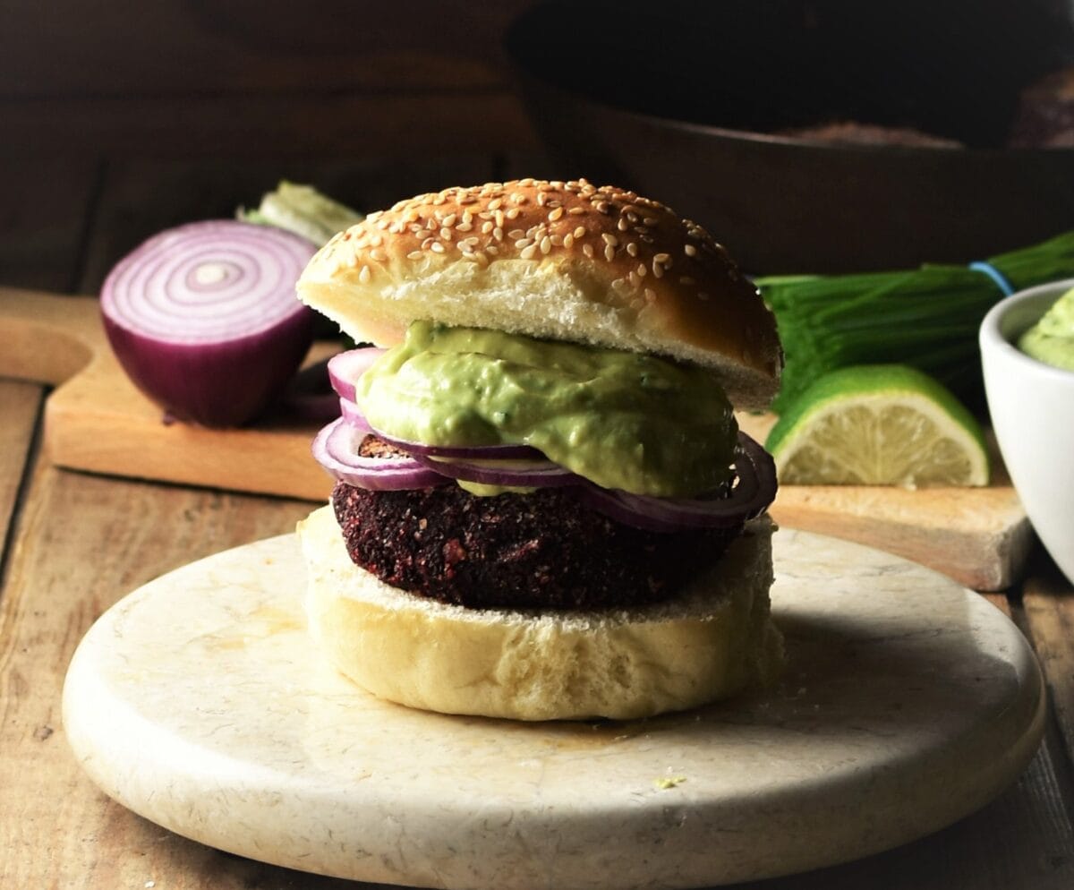 Side view of beet burger on top of marble plate with red onion and lime in background.