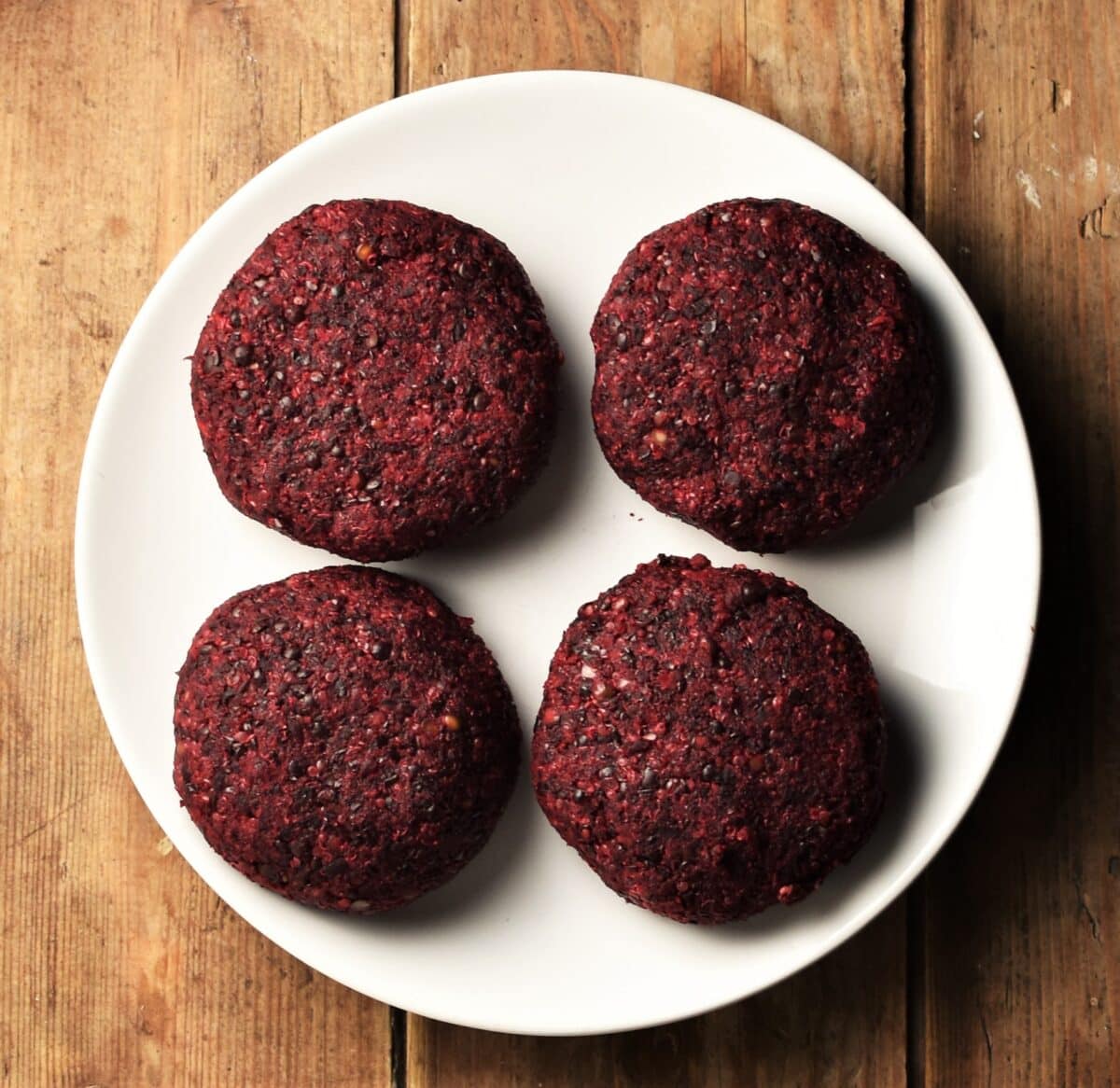 4 uncooked beet quinoa burgers on top of white plate.
