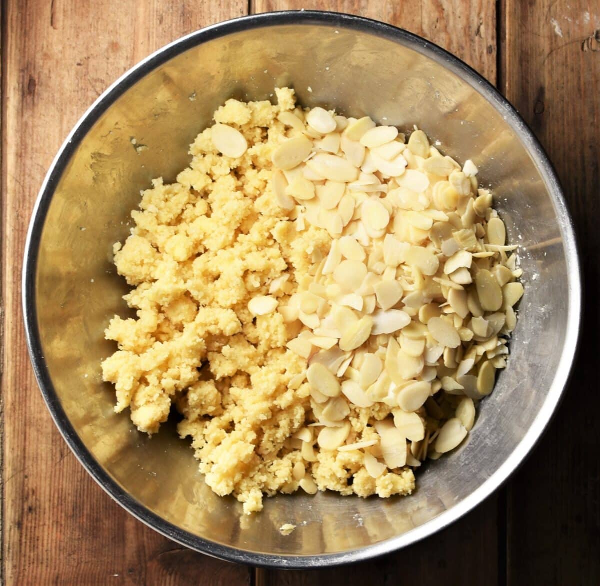 Crumble mixture with flaked almonds in metal bowl.