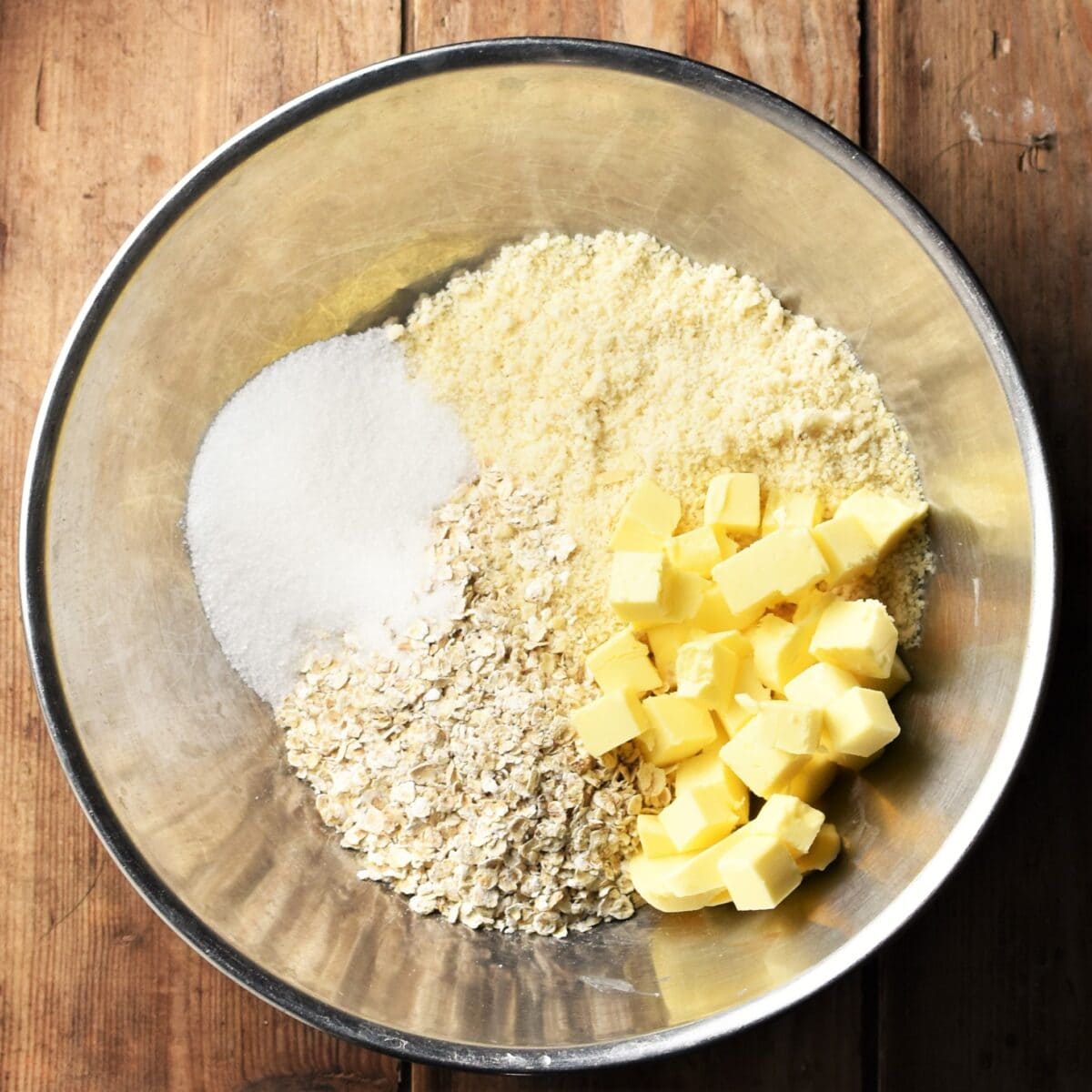 Almond flour, oats, cubed butter and sugar in metal bowl.