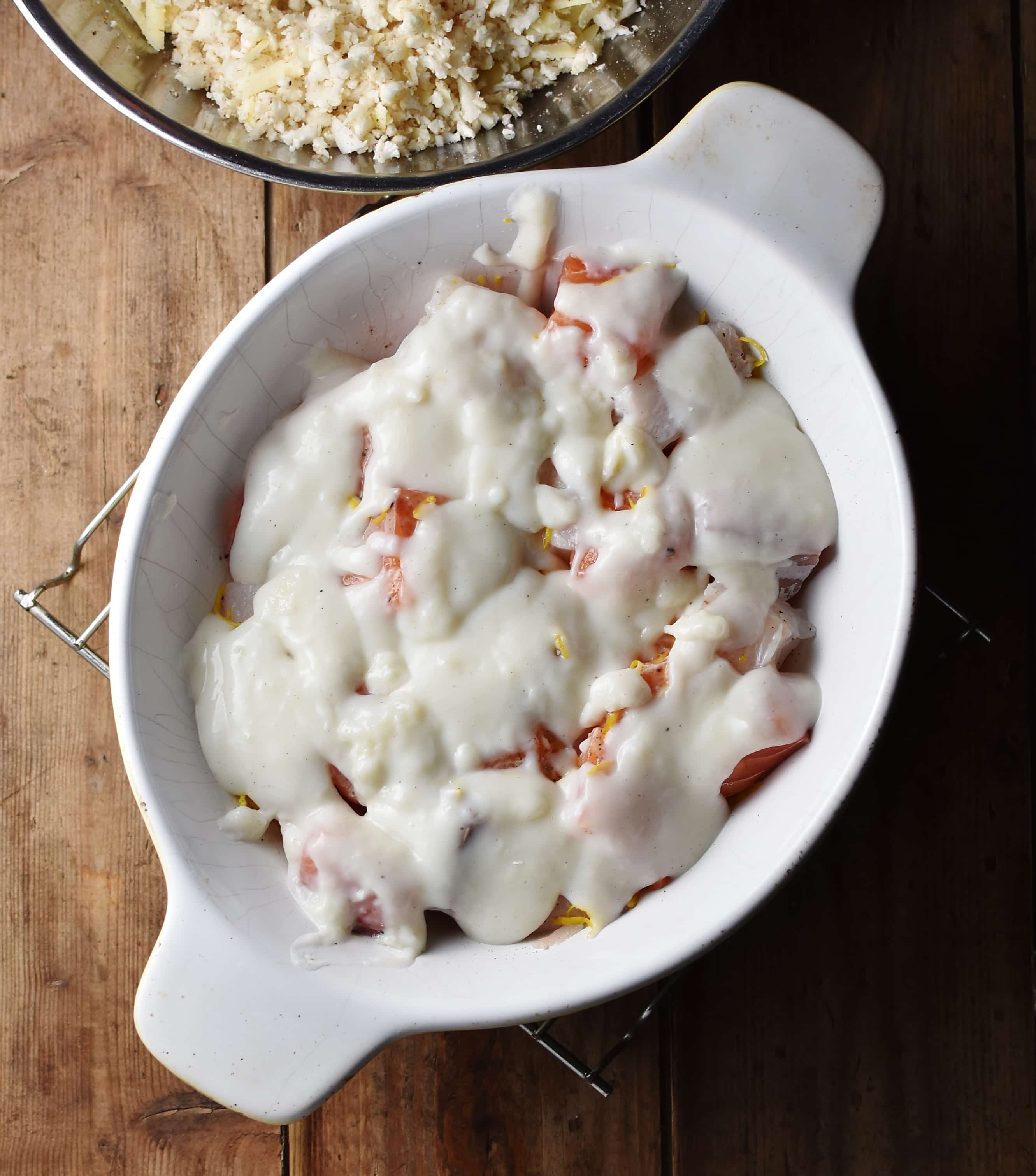 Fish pieces with creamy sauce in white oval dish.
