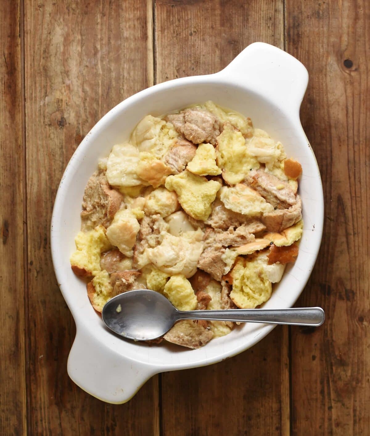 Torn up bread with egg mixture and spoon inside white oval dish.