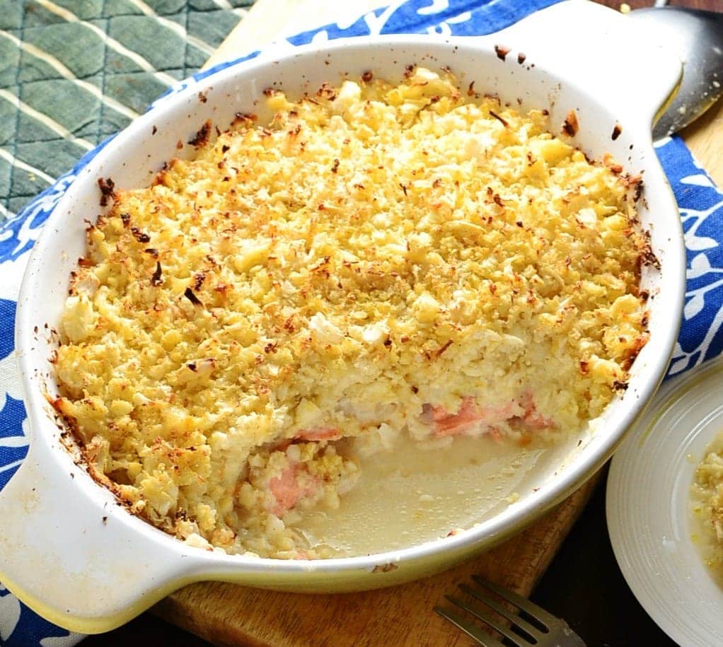 Close-up view of fish pie with cauliflower topping in white oval dish on top of wooden board.