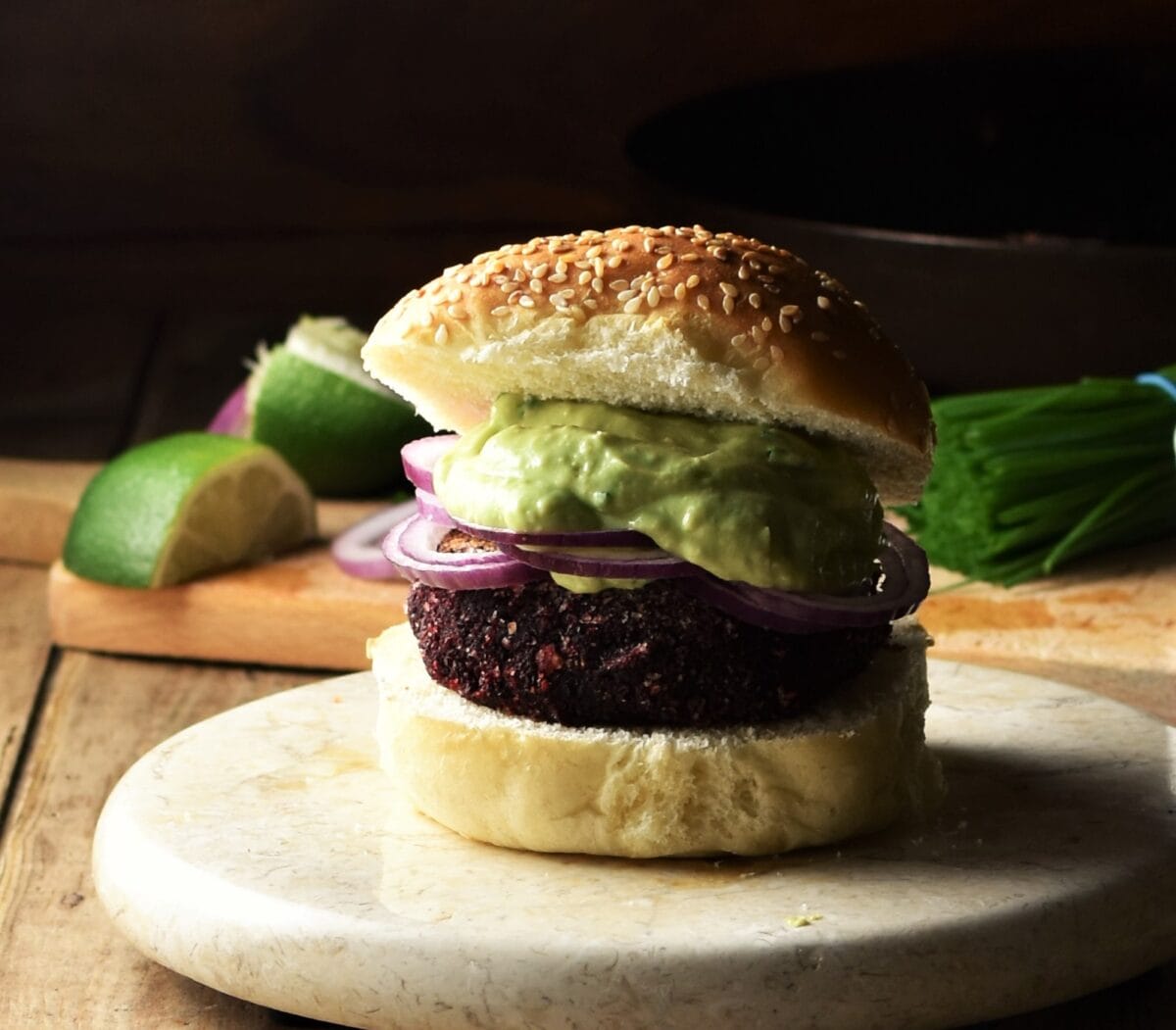 Side view of quinoa beet burger on top of marble plate with lime and chives in background.