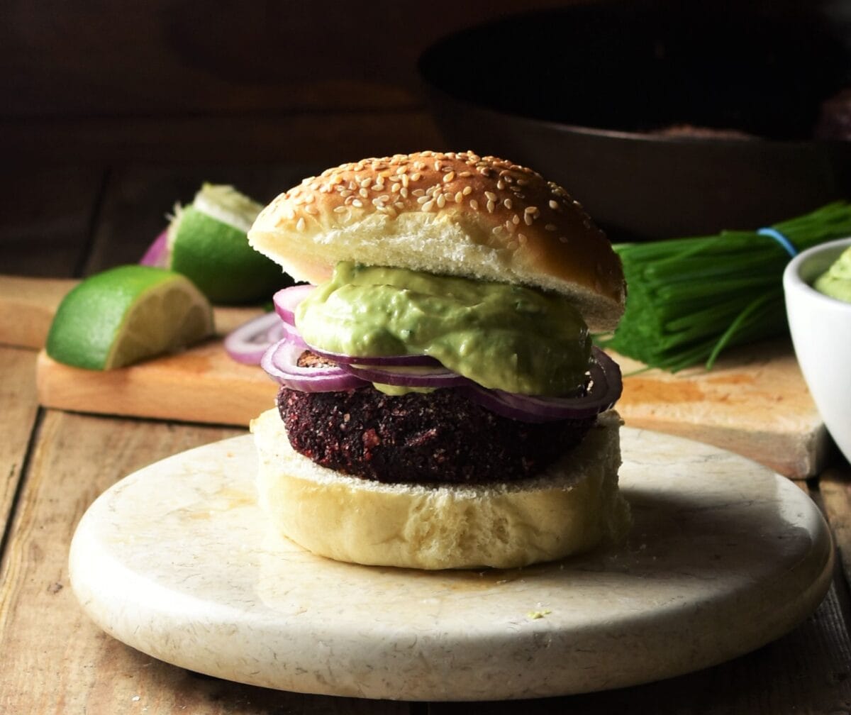 Side view of quinoa beetroot burger on top of marble plate with lime and chives in background.