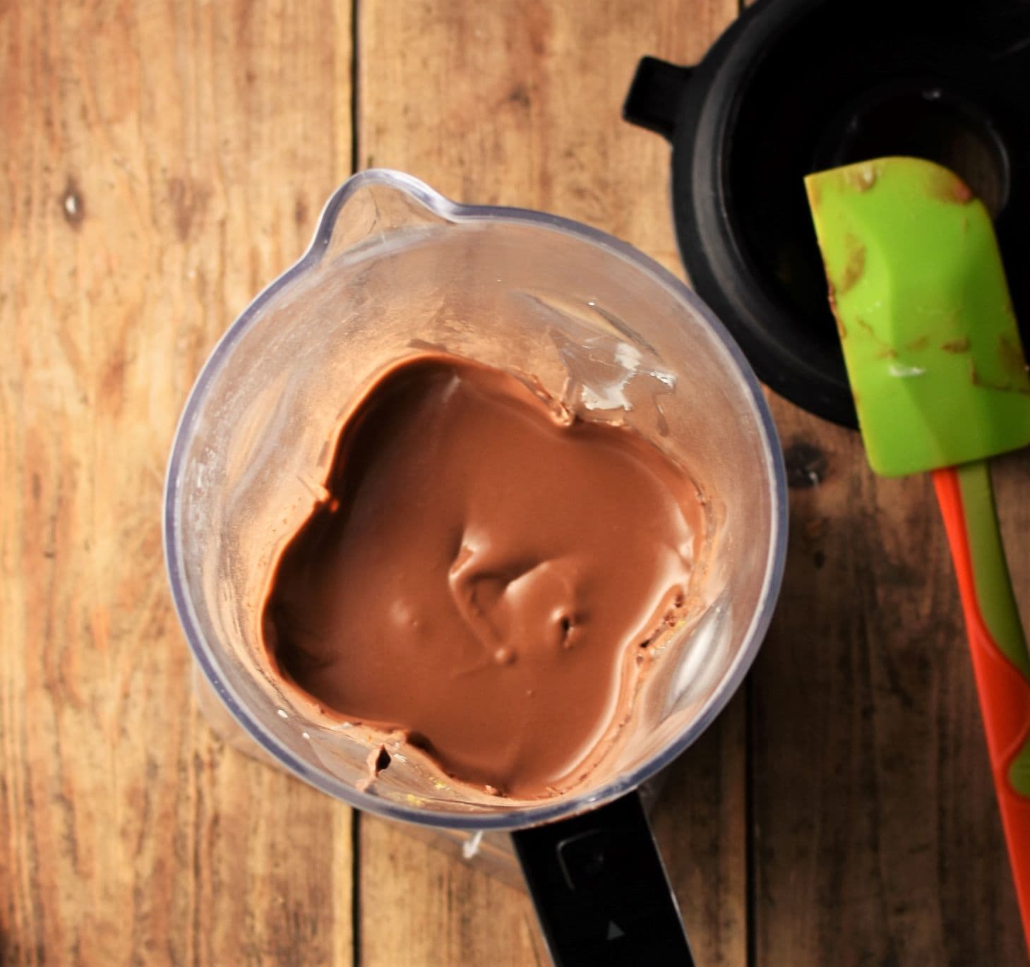 Top down view of chocolate mousse in blender, with blender top and green spatula in top right corner.