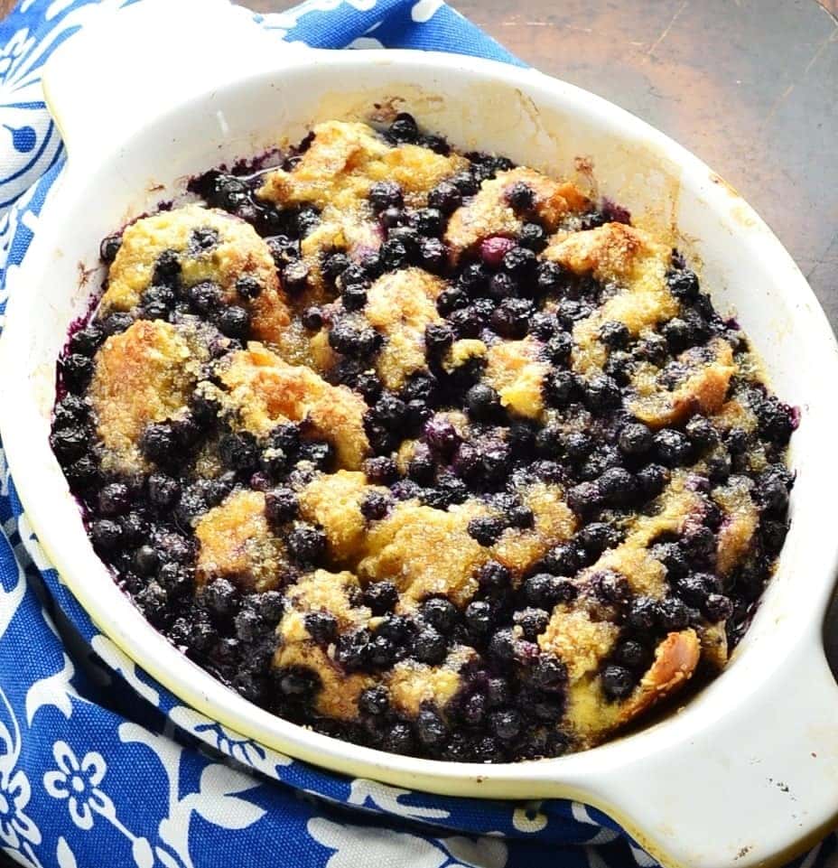 Blueberry french toast in white oval dish and blue-and-white cloth to left.