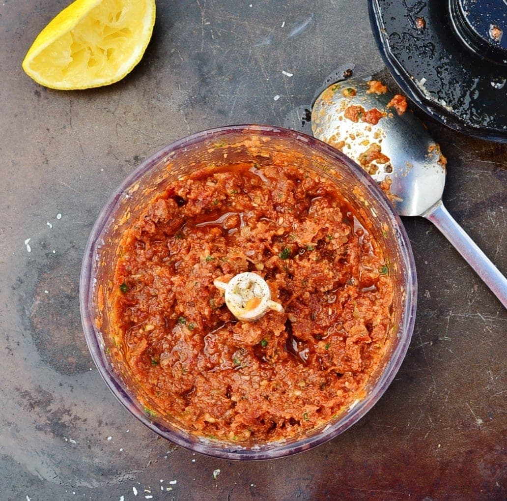 Top down view of sun dried tomato pesto mixture in blender with spoon and lemon half.