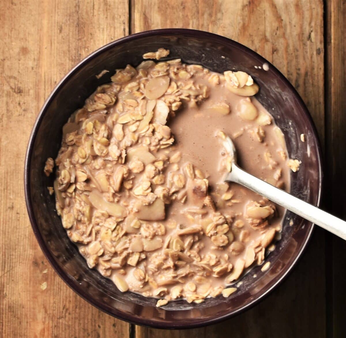 Oats mixture with milk and cocoa in bowl with spoon.