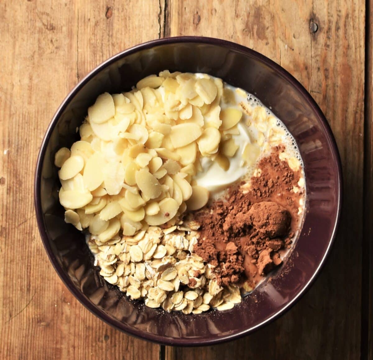 Oats, flaked almonds, milk and cocoa in bowl.