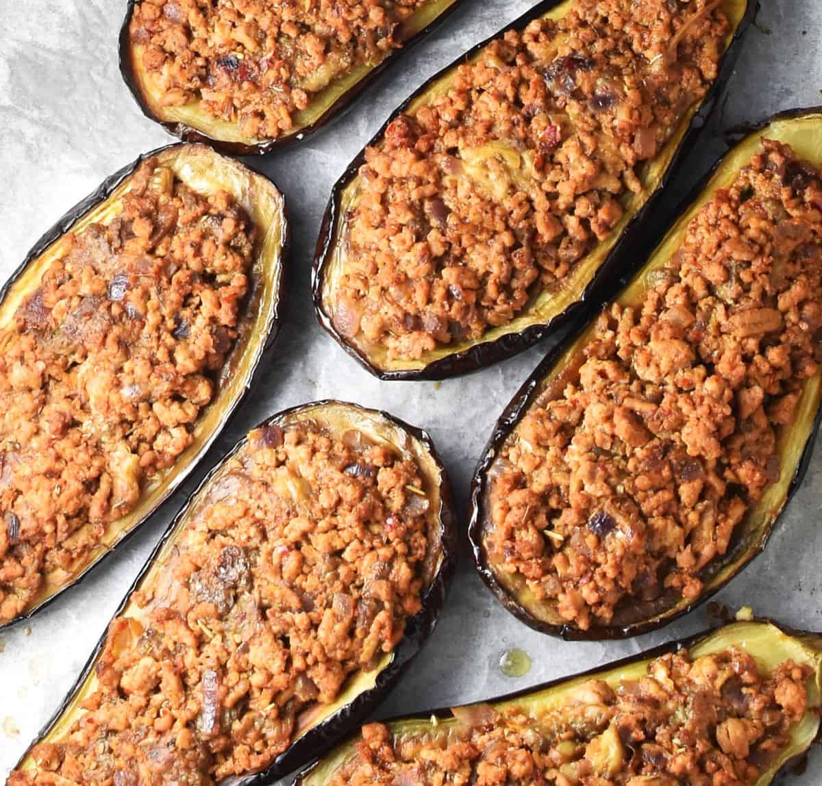 Top down view of baked turkey stuffed eggplant halves on top of parchment paper.