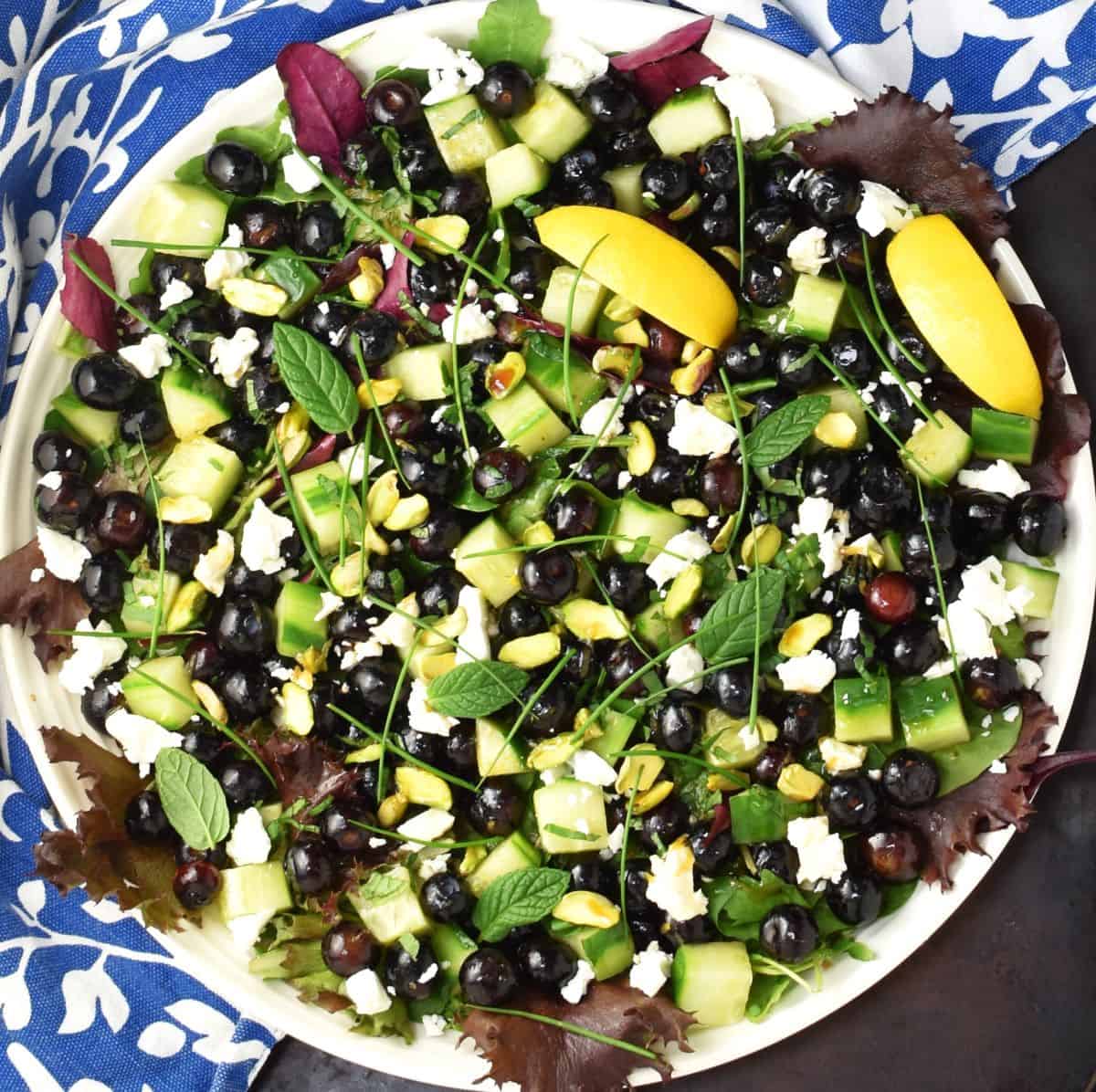 Top down view of assembled blueberry salad with cucumber and lemon wedges.