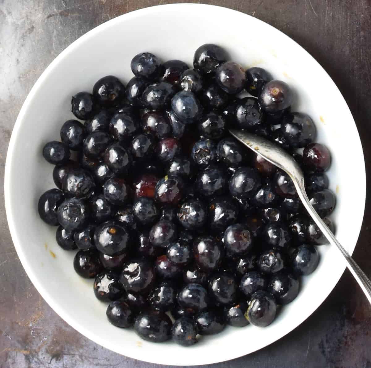 Blueberries with spoon in white bowl.