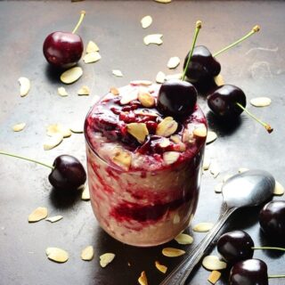 Cherry overnight oats with fresh cherries, almond flakes and spoon on dark brown surface.