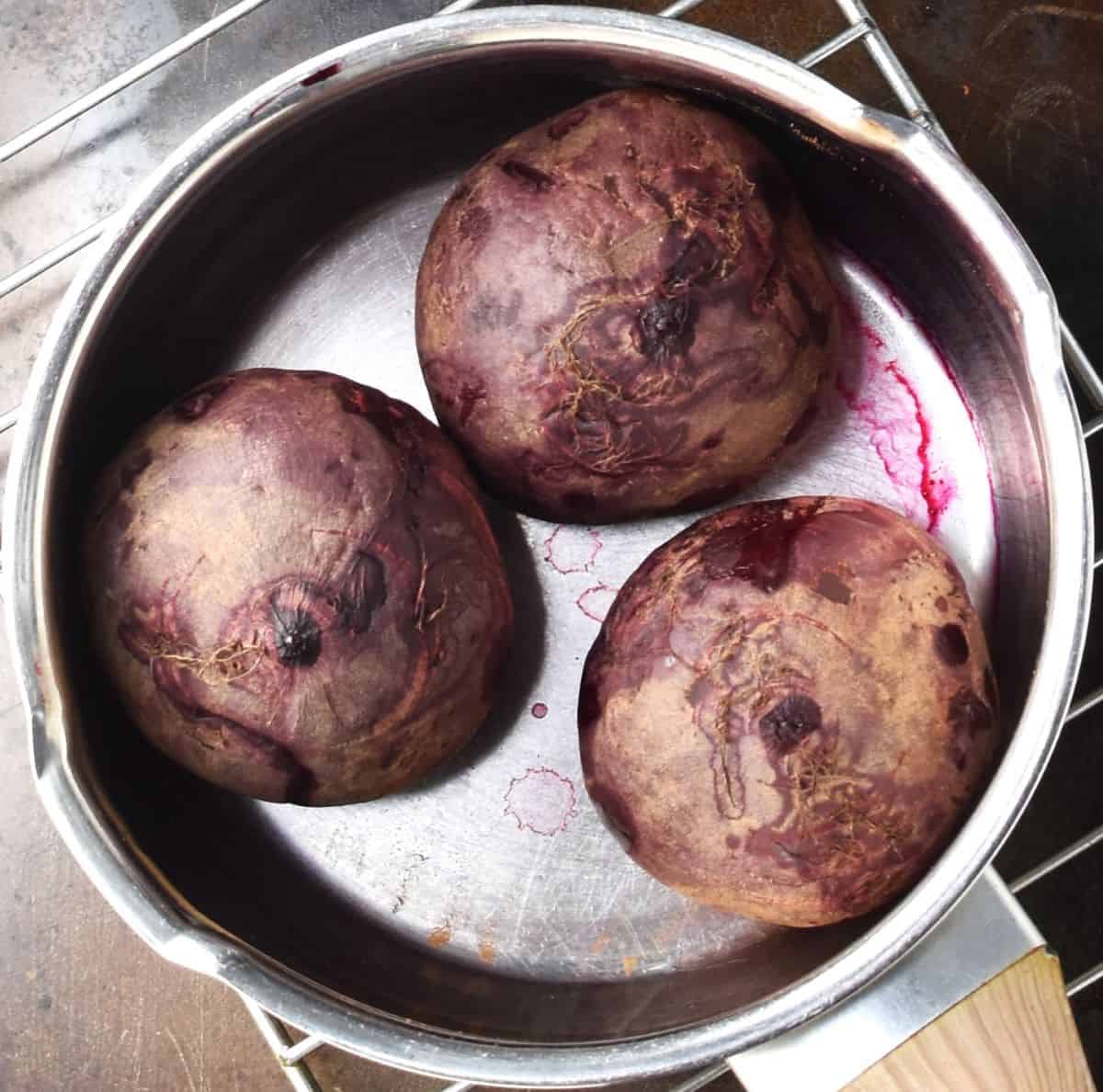 Top down view of 3 cooked unpeeled beets in pot.
