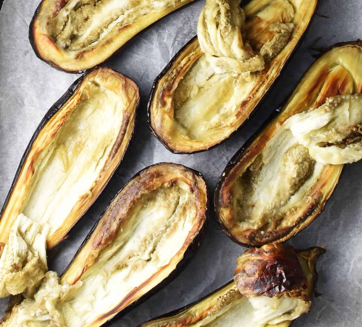 Roasted eggplant halves with scooped out pulp on parchment.