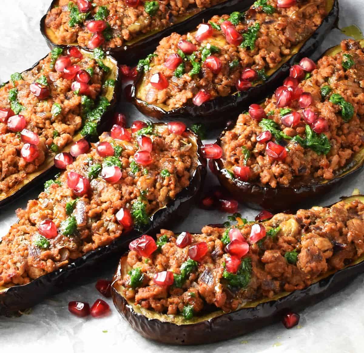 Close-up side view of stuffed eggplants with ground turkey, garnished with parsley drizzle and pomegranate seeds.