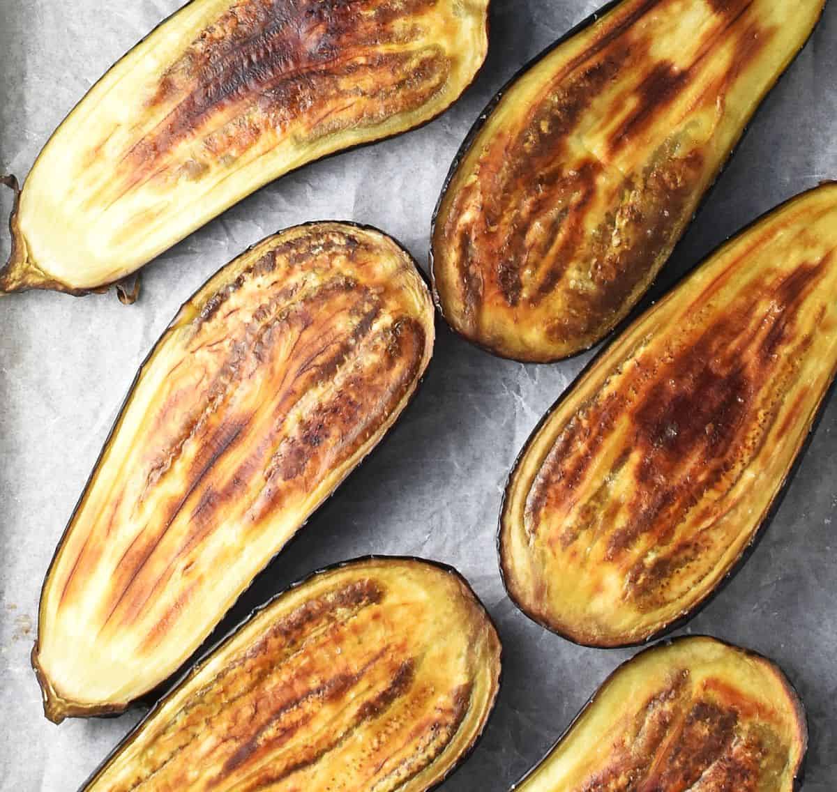 Top down view of roasted browned eggplant halves on parchment.