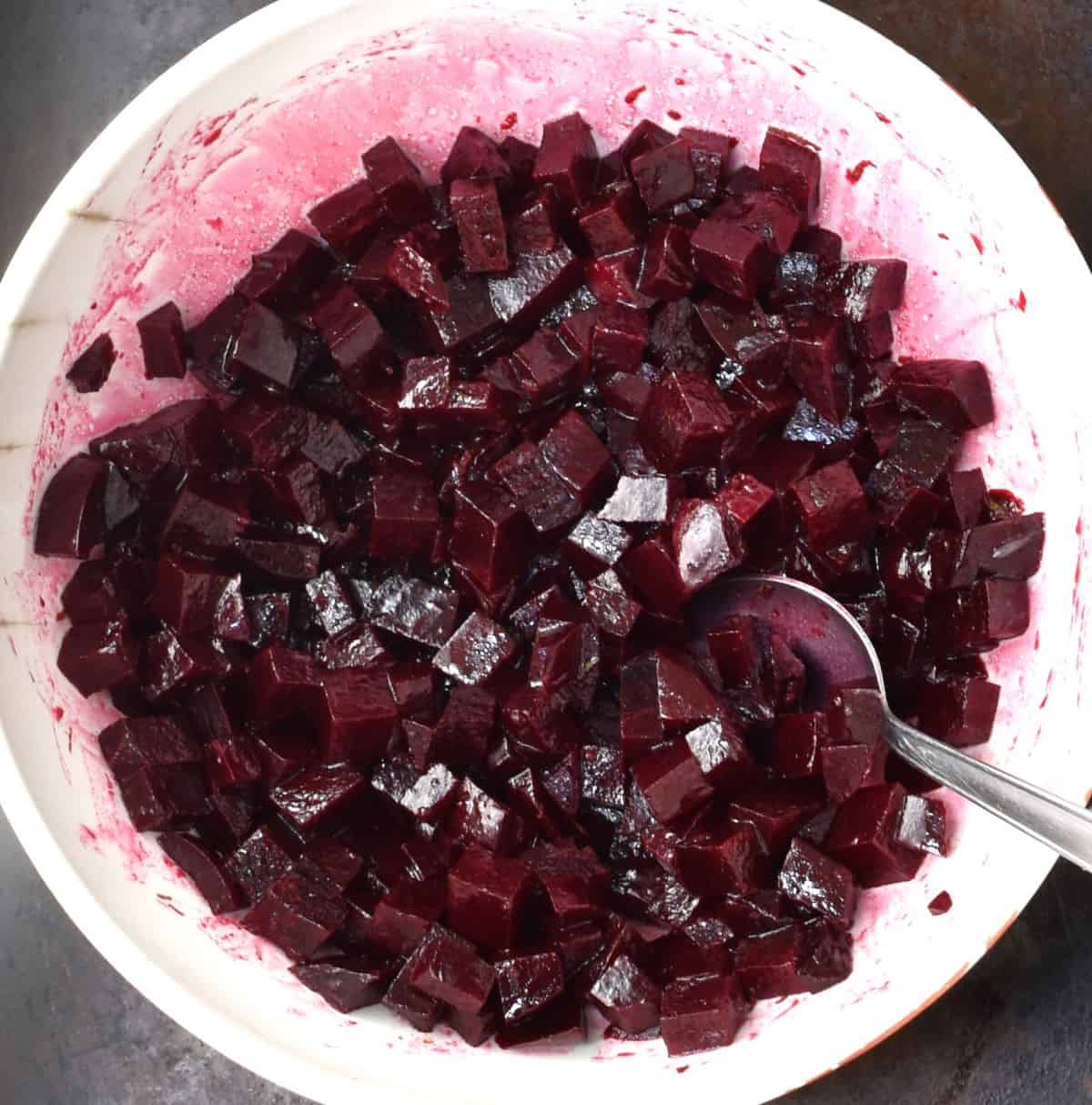 Cubed beets marinating in white bowl with spoon.