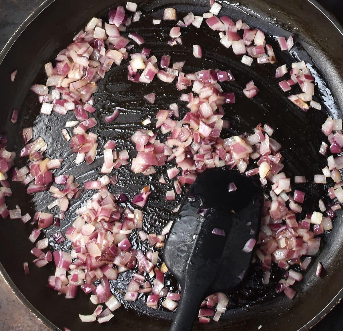 Cooking chopped red onion in large pan with back spoon.