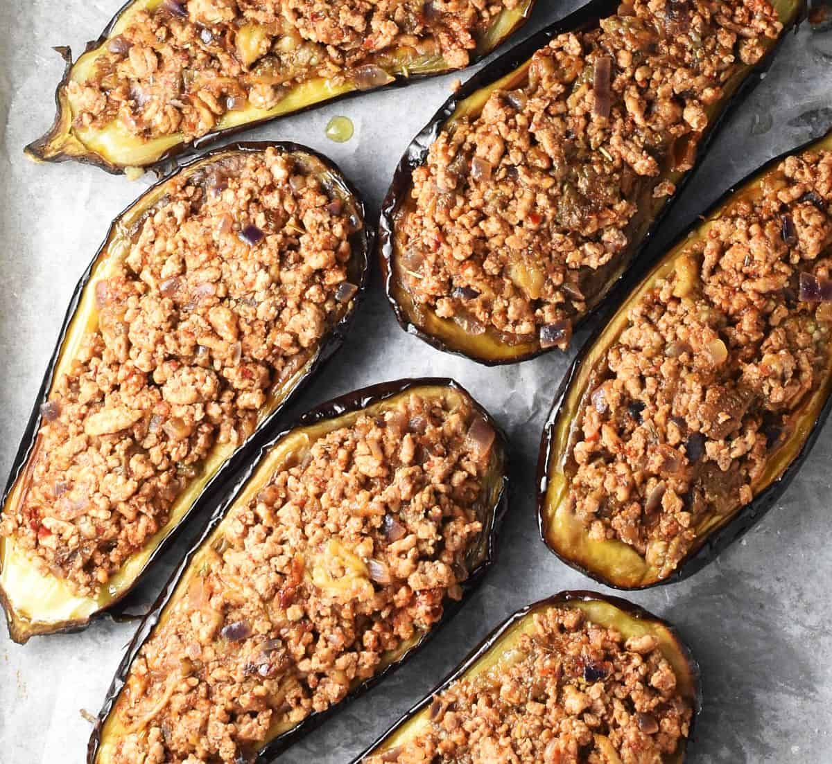 Stuffed eggplant halves with ground turkey filling on parchment.