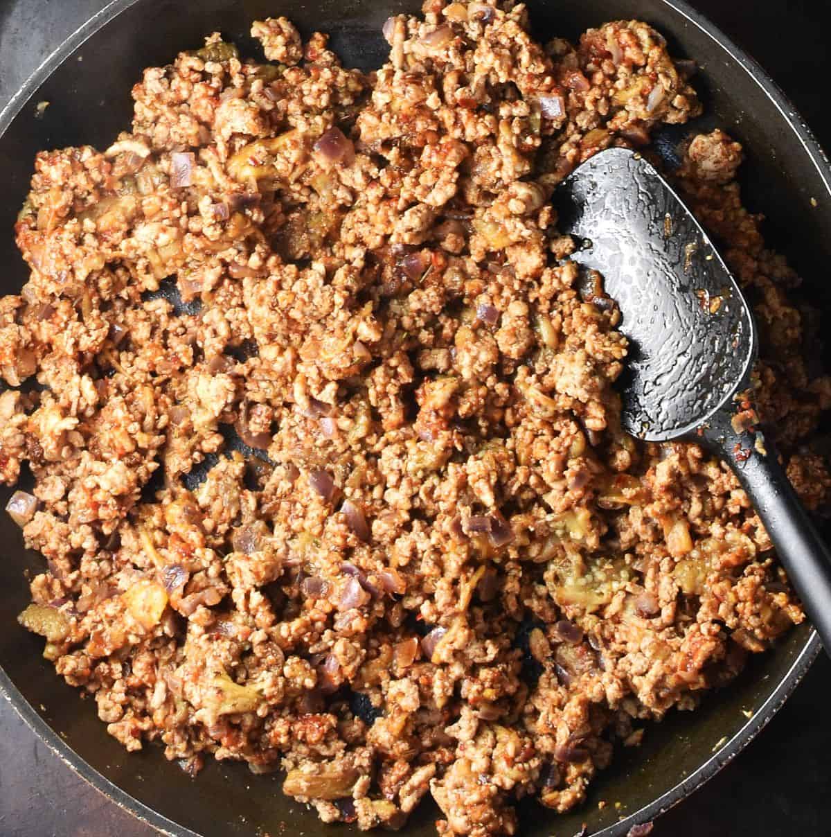 Ground turkey eggplant stuffing mixture with black spoon in large pan.