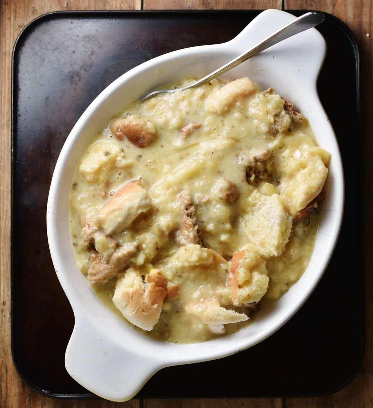 Top down view of torn bread with egg mixture and fork inside oval white dish.