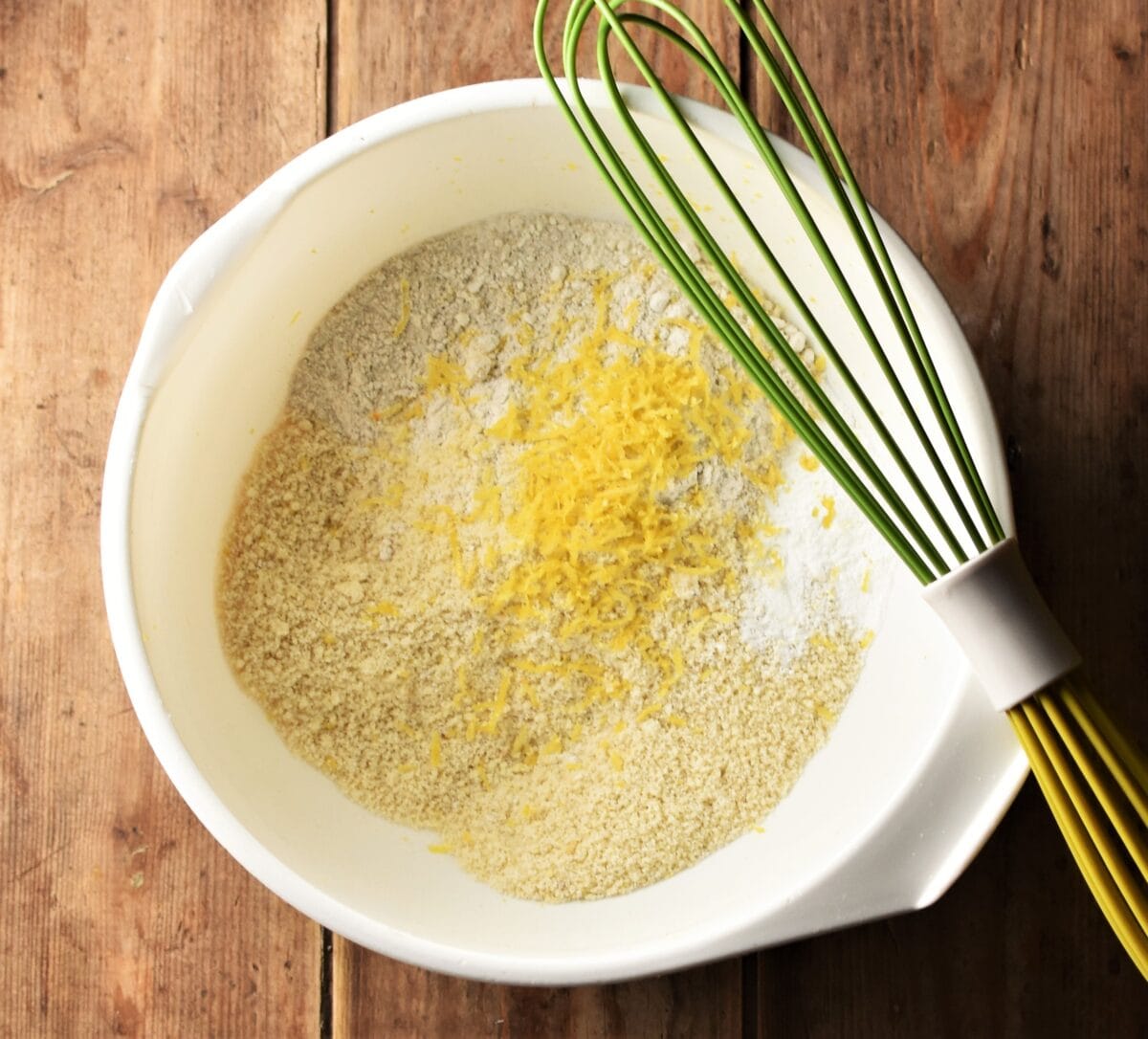 Flour and lemon zest in large white bowl with green whisk.