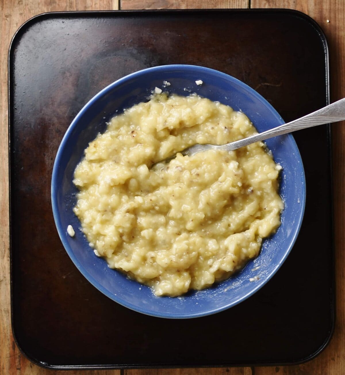 Mashed banana with fork inside blue bowl.