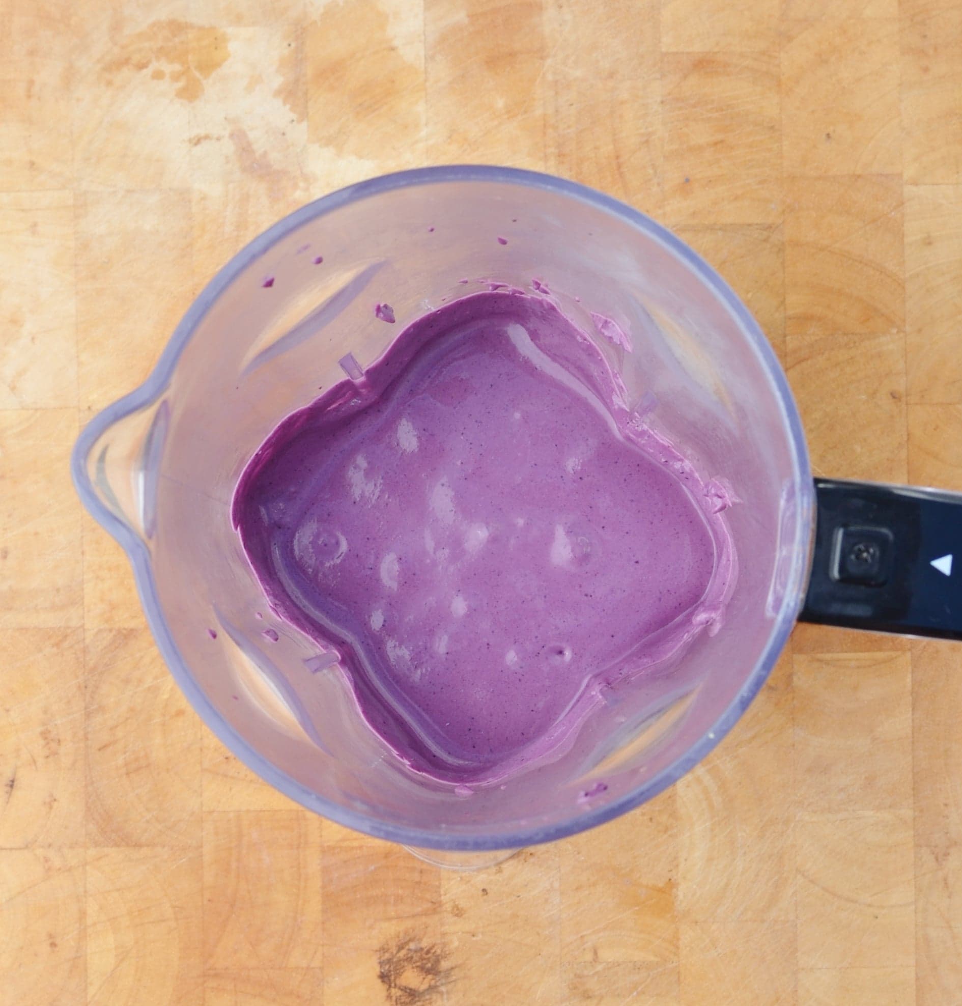 Blueberry cream cheese dessert mixture in blender on light wooden surface.