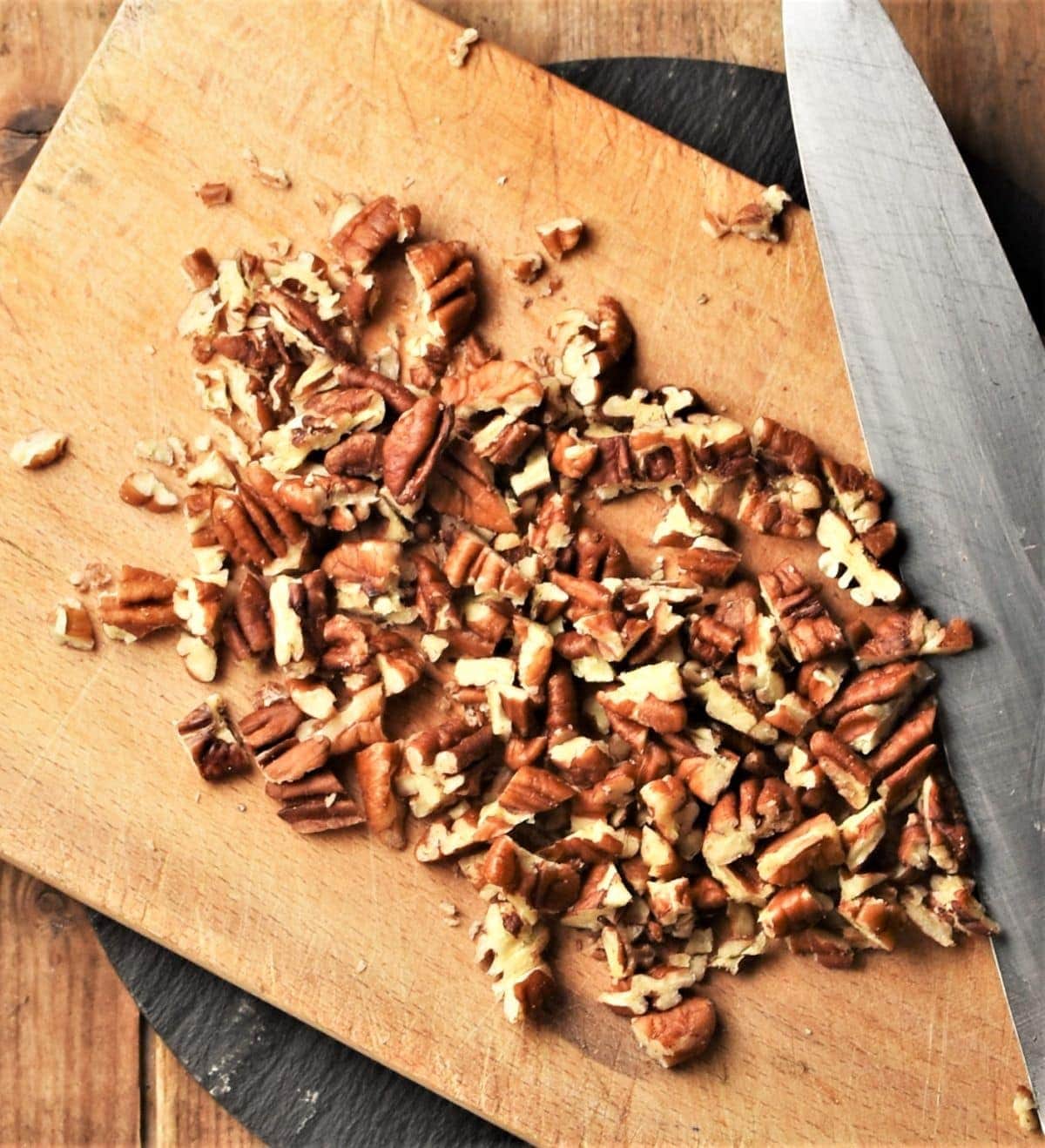 Chopped pecans with knife on top of cutting board.
