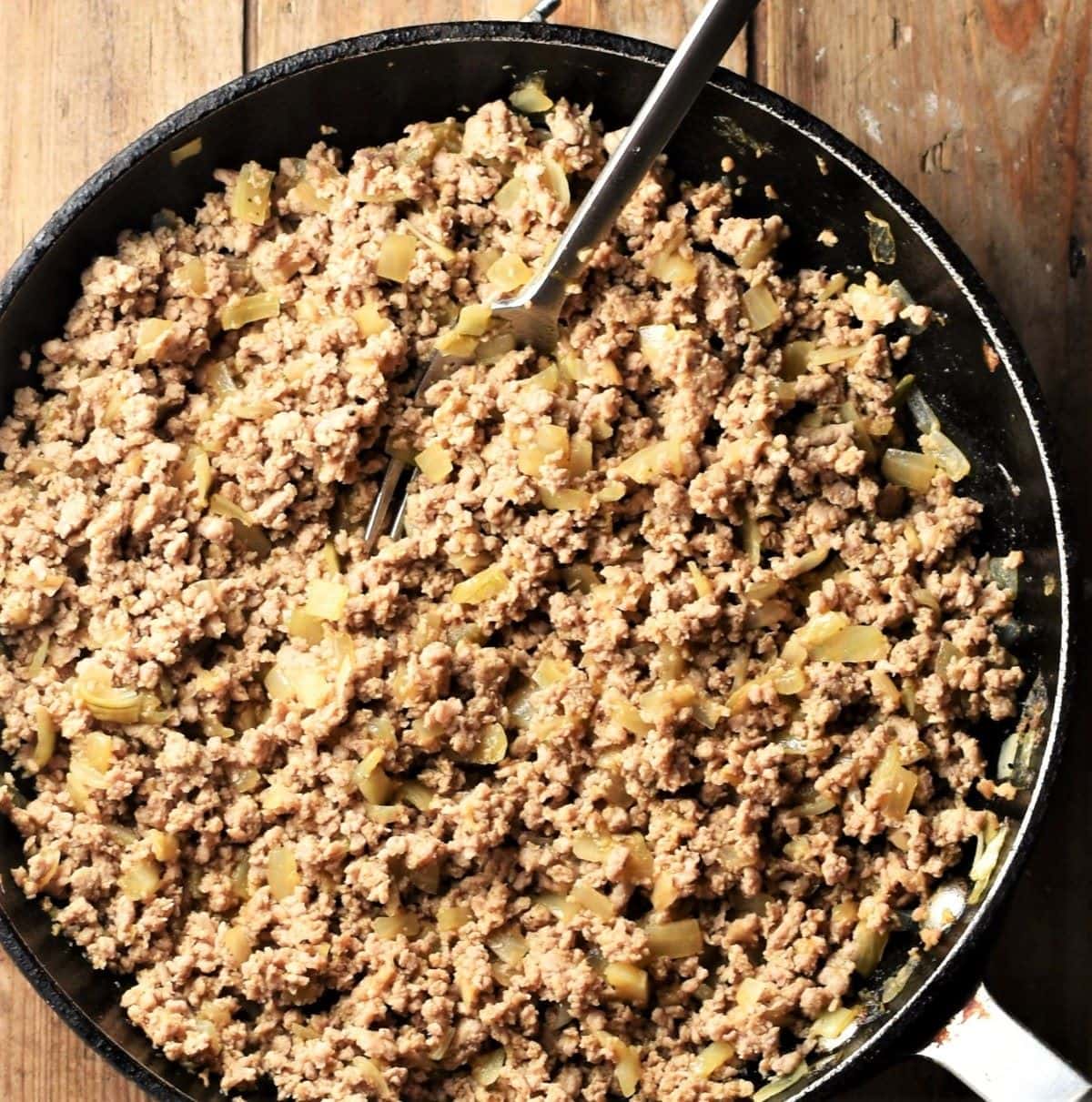 Cooked ground meat with onion mixture in large pan with fork.