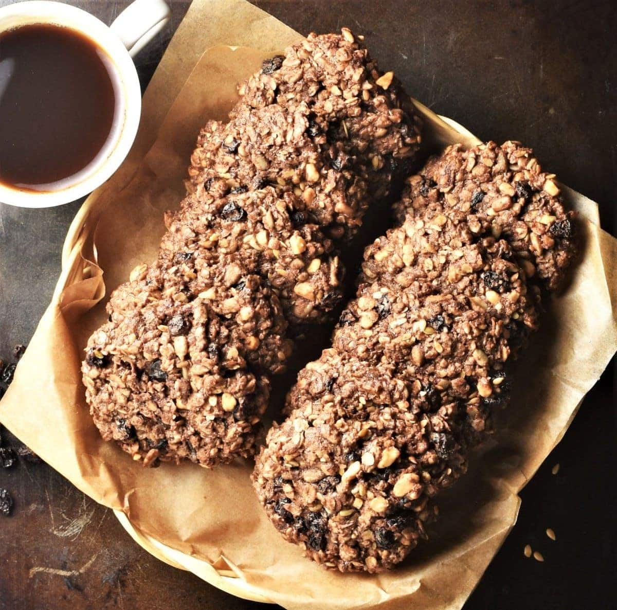 Top down view of chocolate oatmeal cookies stacked inside dish with parchment and coffee in cup.