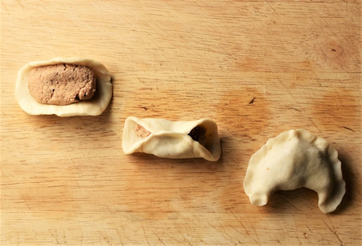 Making pierogi with meat on top of wooden surface.