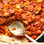 Top down partial view of butternut squash, tomatoes and green olives in large shallow white dish with large spoon.